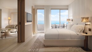 Moderni hotellihuone, jossa on suuri sänky, televisio, merinäköalalla varustettu parveke ja pieni oleskelualue.