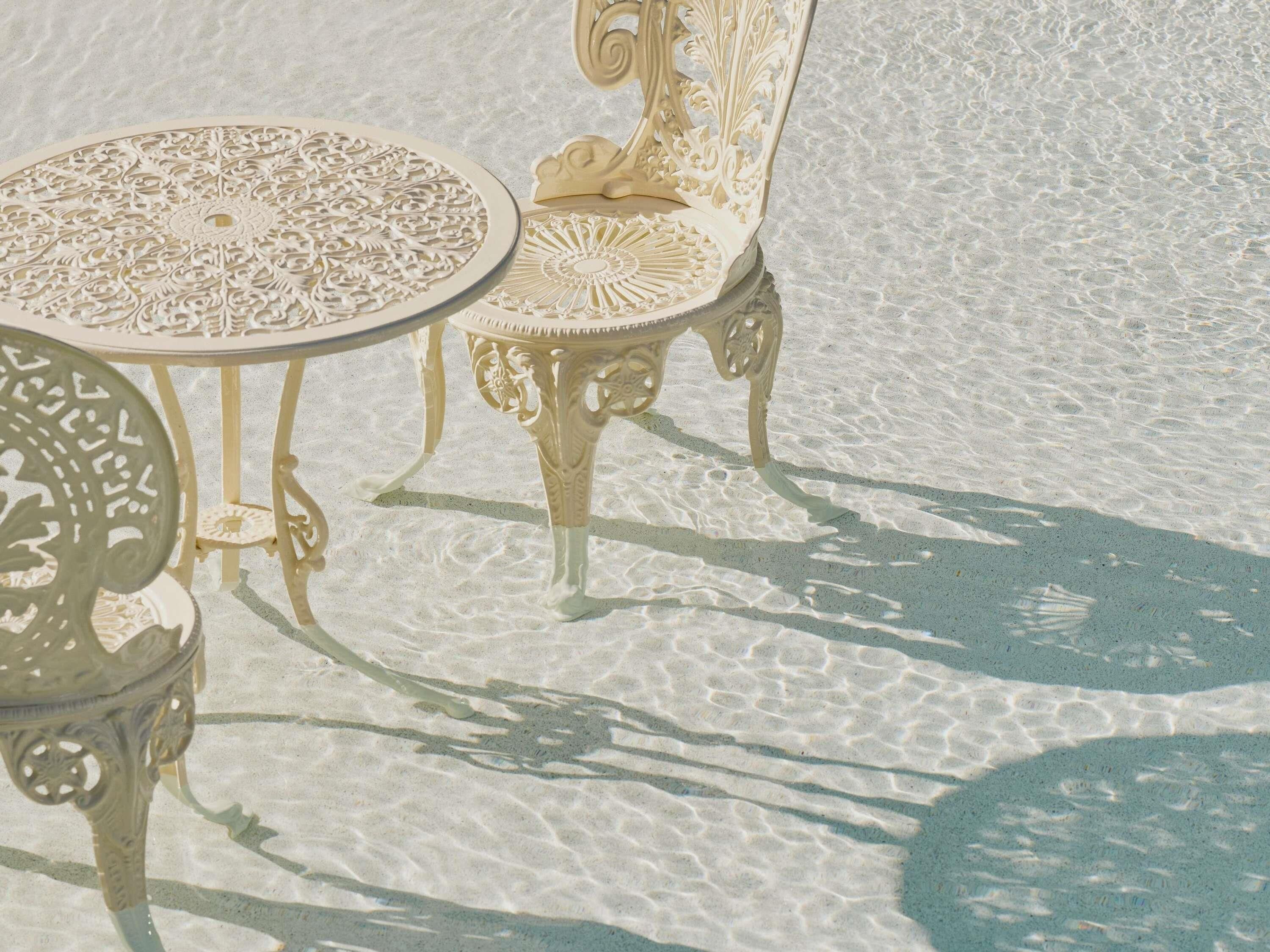 A beachside seating area with ornate metal chairs and a table, featuring intricate designs.