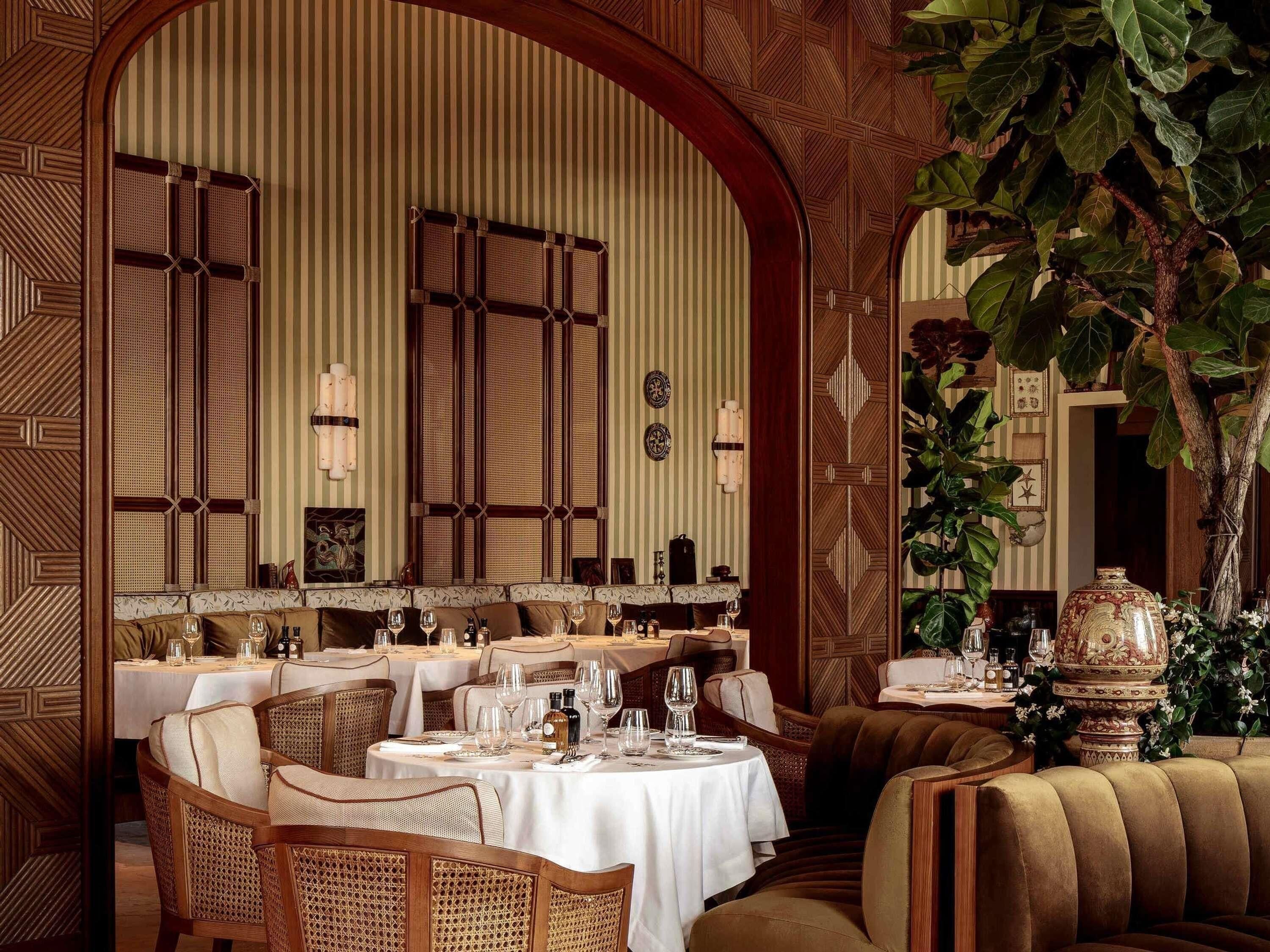 A restaurant interior with high-backed chairs, round tables, and a large mirror.