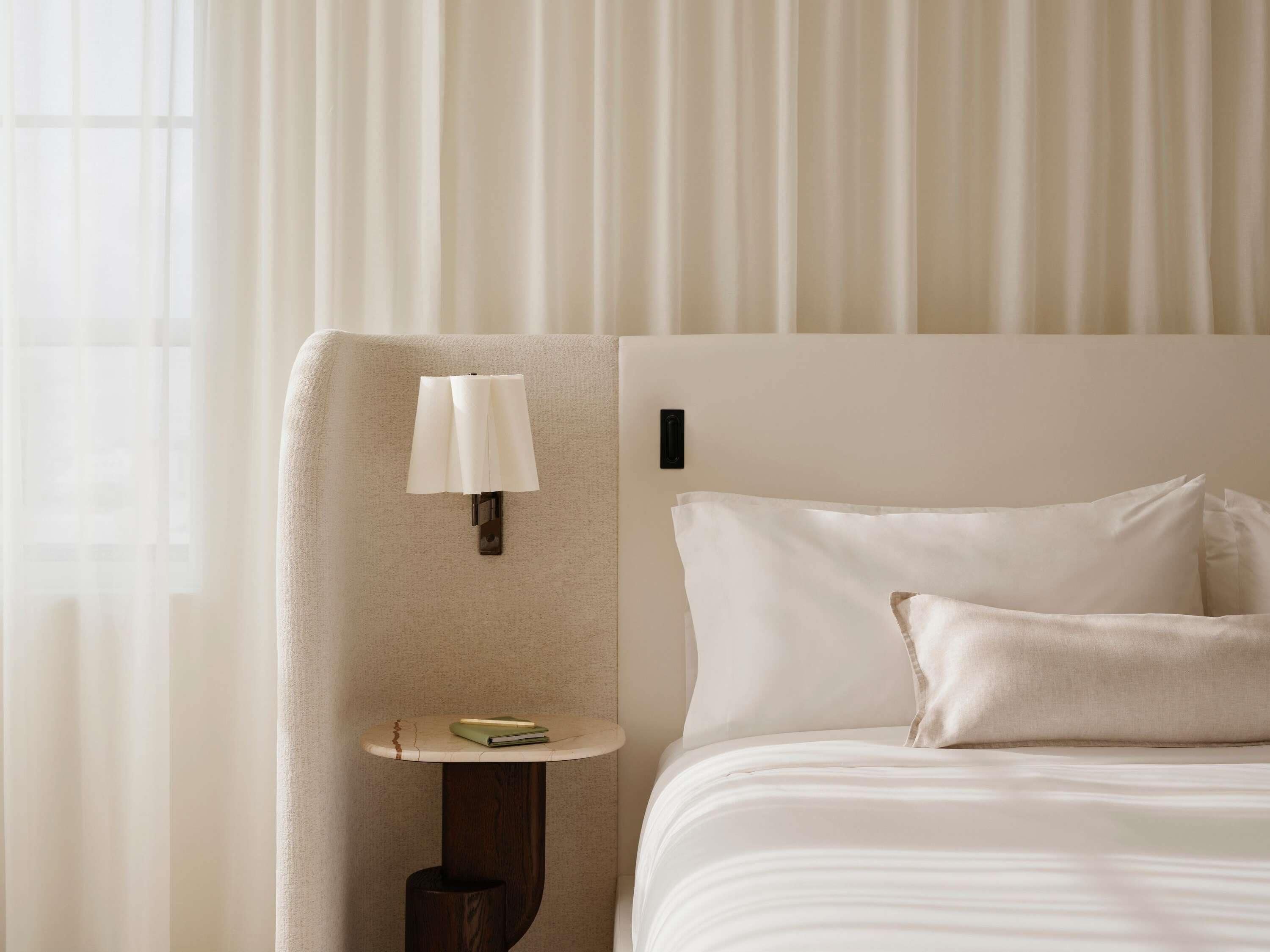 Een hotelkamer met een bed, nachtkastje, lamp en raam met gordijnen.