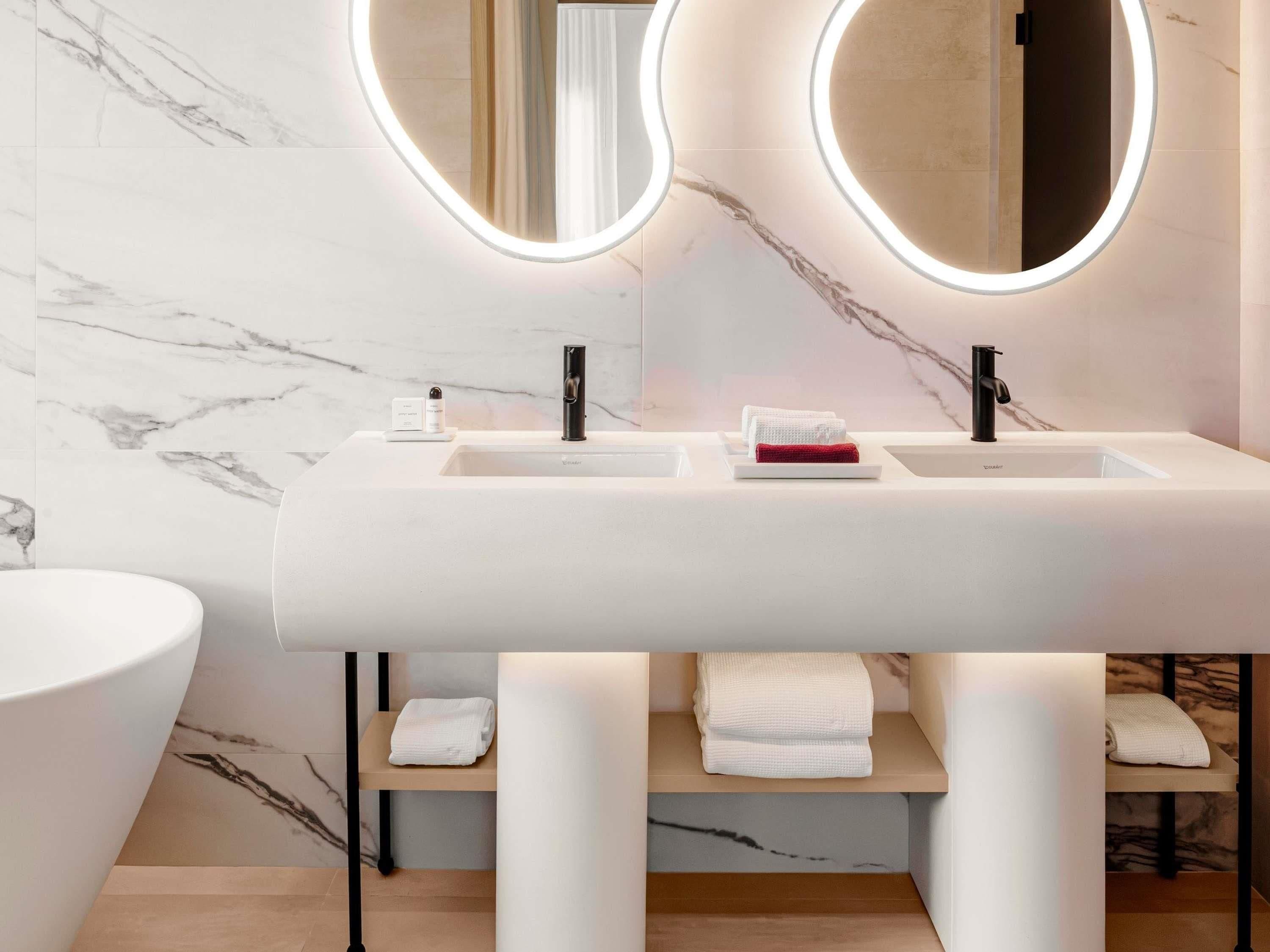A modern bathroom with two sinks, a large mirror with integrated lighting, and marble-patterned walls.