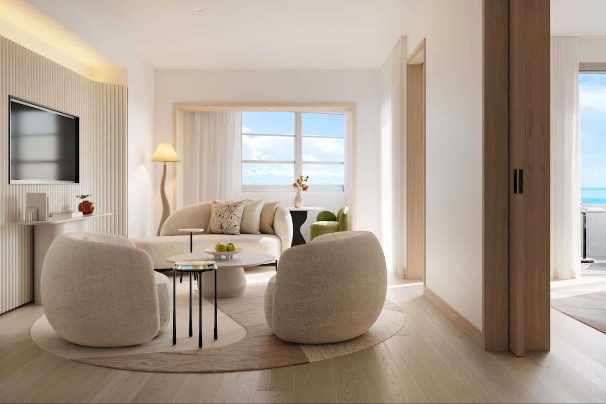A modern living room with a sofa, two armchairs, a coffee table, a TV, and a large window with a view.
