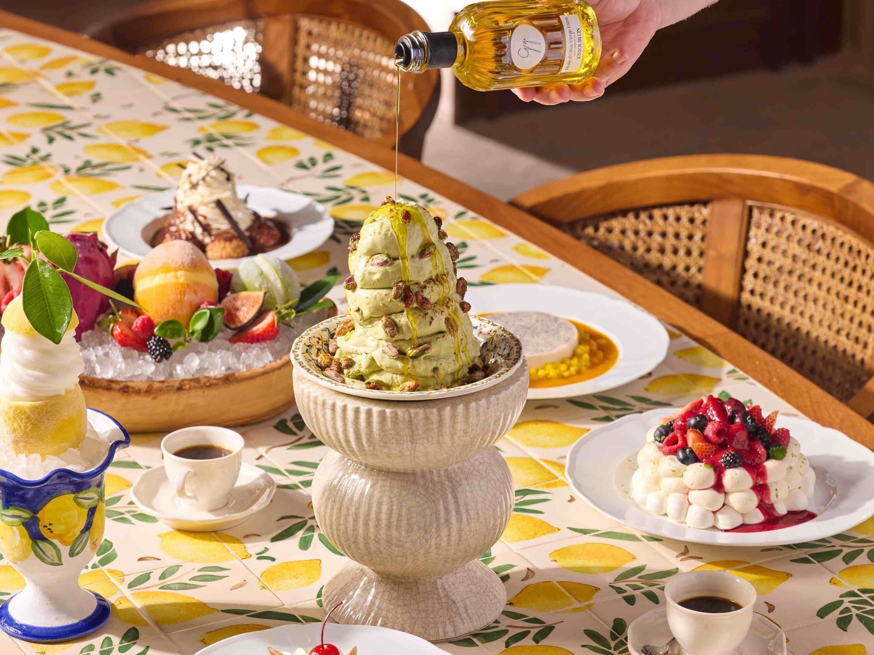A table set with various desserts, including a layered ice cream dessert, a fruit-topped dessert, and a dessert with nuts.