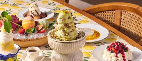 A table set with various desserts, including a layered ice cream dessert, a fruit-topped dessert, and a dessert with nuts.