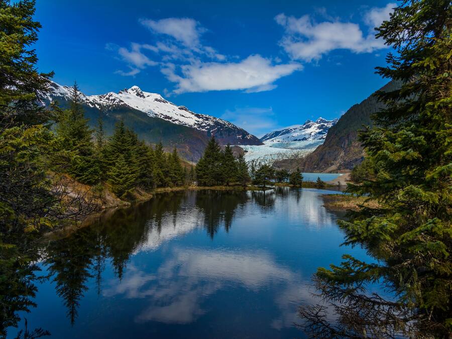 A serene lake surrounded by snow-capped mountains and dense forest.