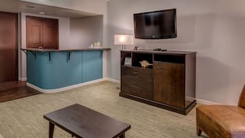 A modern living room with a dark wooden coffee table, a blue accent wall, a flat-screen TV mounted above a wooden cabinet, and a small ottoman.
