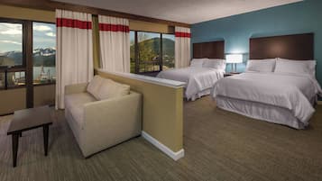 A hotel room with two beds, a sofa, a small table, and a view of mountains through large windows.
