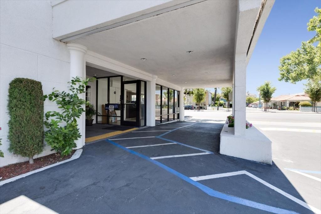 Entrada d'un edifici amb un passadís cobert, cel serè i zona d'aparcament.
