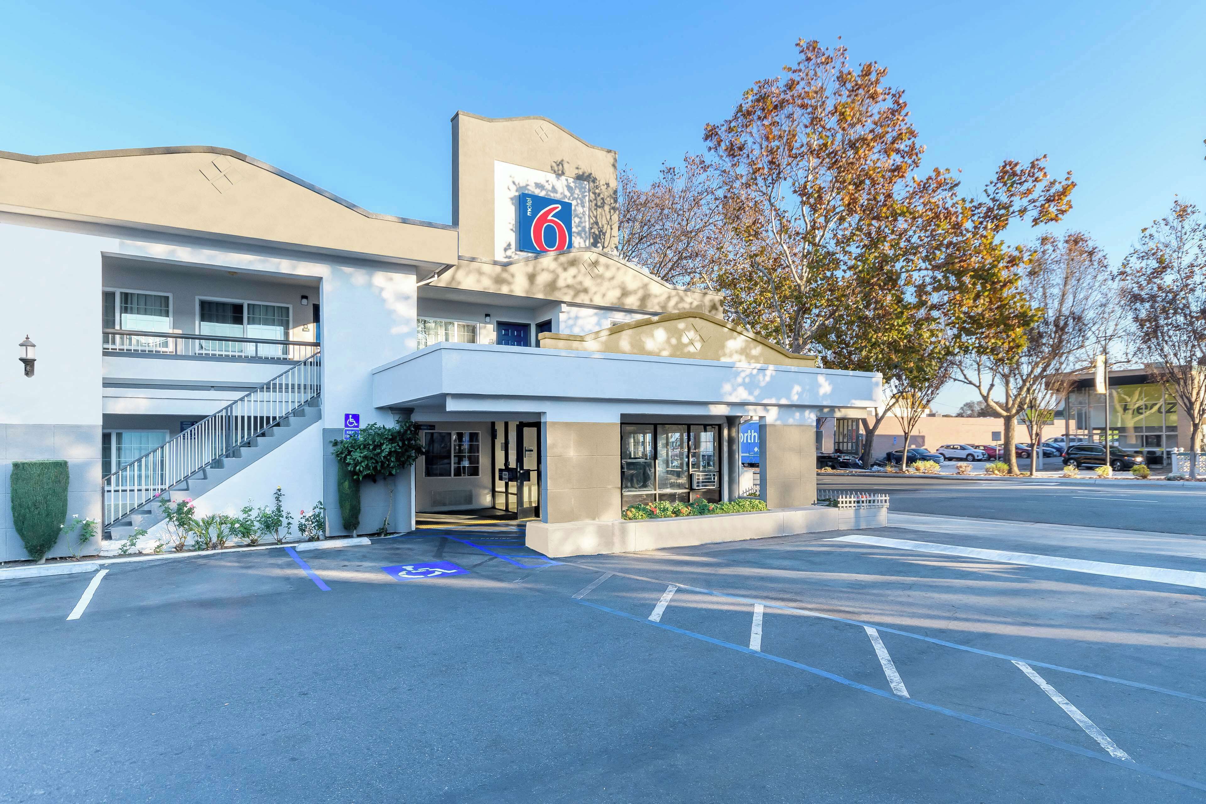 A modern hotel with a '6' sign, accessible entrance, and a parking lot.