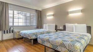 Habitación de hotel con dos camas, una ventana con cortinas, un radiador y una lámpara fijada a la pared.