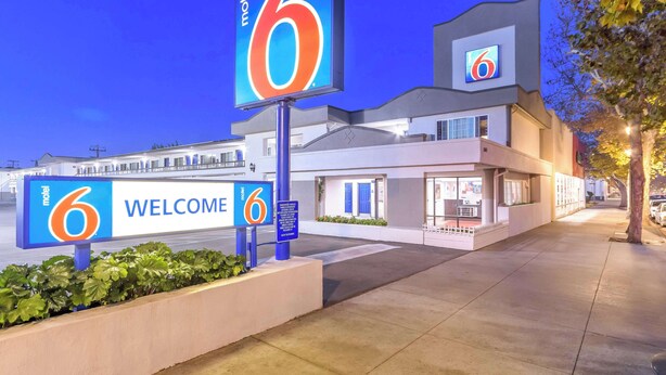 Un motel con un llamativo letrero con el número '6', un cartel de 'BIENVENIDOS' y una fachada de edificio moderna.