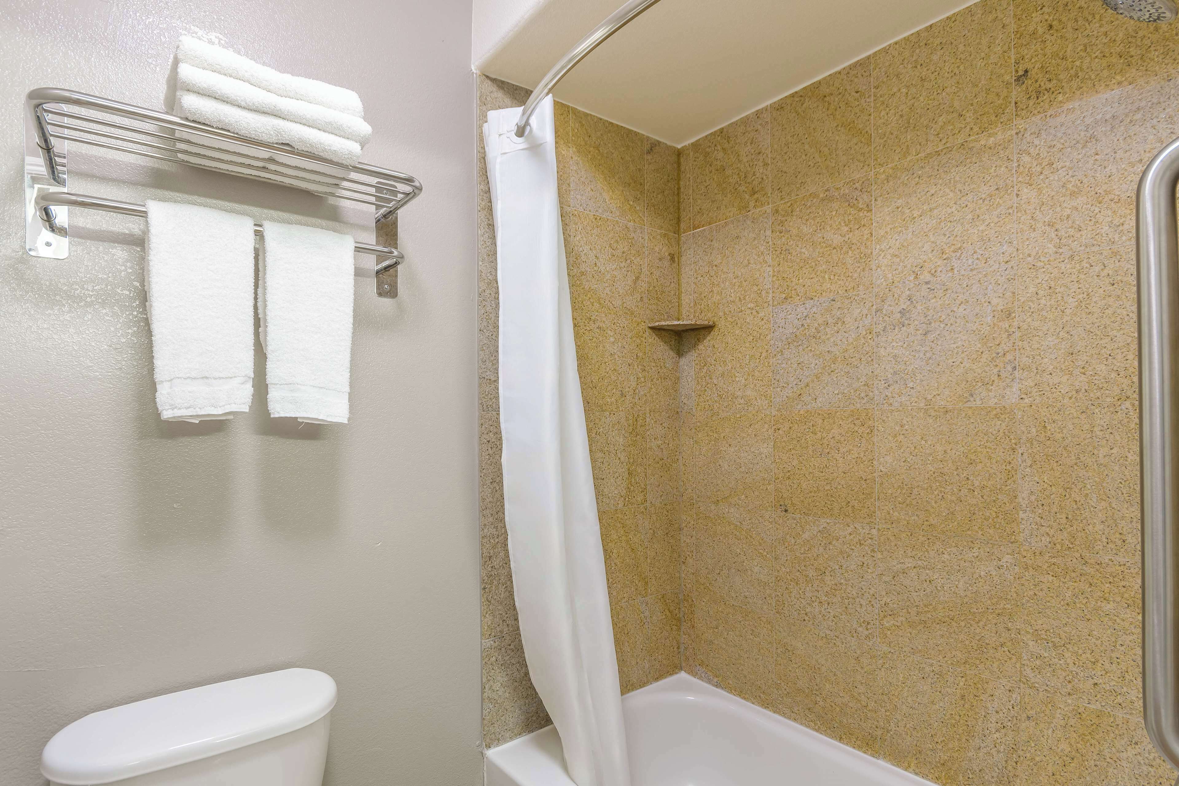 A bathroom with a toilet, a towel rack with towels, a shower with a curtain, and tiled walls.
