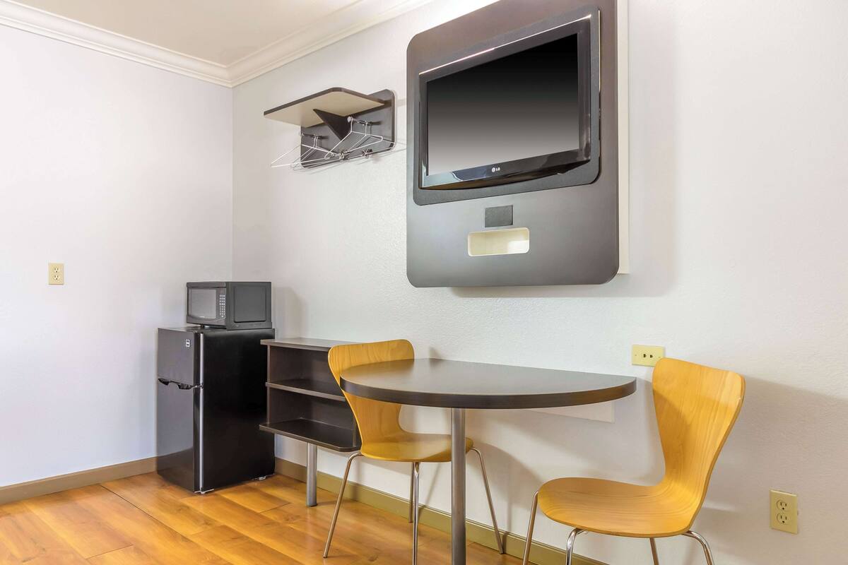 A compact kitchen with a refrigerator, microwave, and a flat-screen TV mounted on the wall.