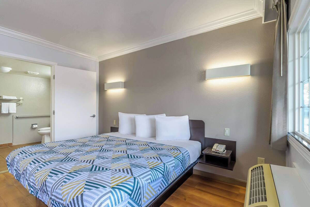 A hotel room with a large bed, a bedside table with a phone, a wall-mounted light, and a window with curtains.