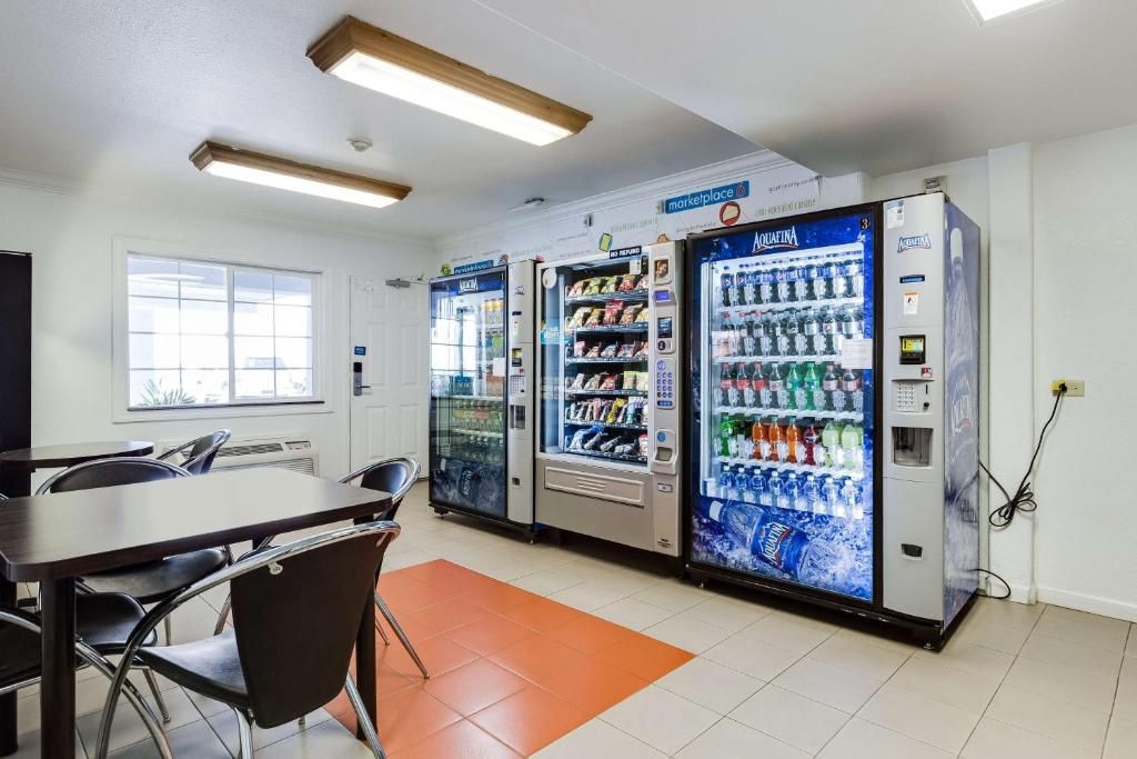 A room with a table and chairs, three beverage vending machines, and a window.