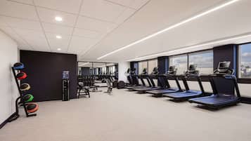 Un gimnasio con cintas de correr, bicicletas estáticas y un dispensador de agua.