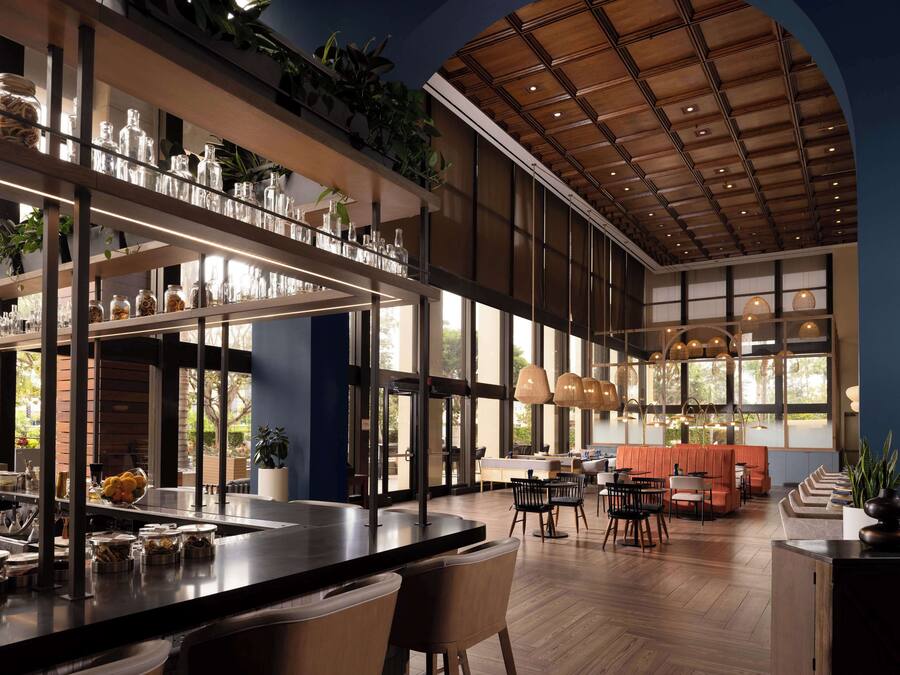 A modern restaurant with a bar area, seating, and large windows.