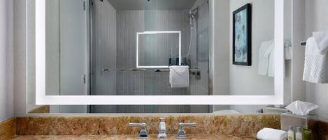 A bathroom with a granite countertop, a sink, a mirror, and a shower area.