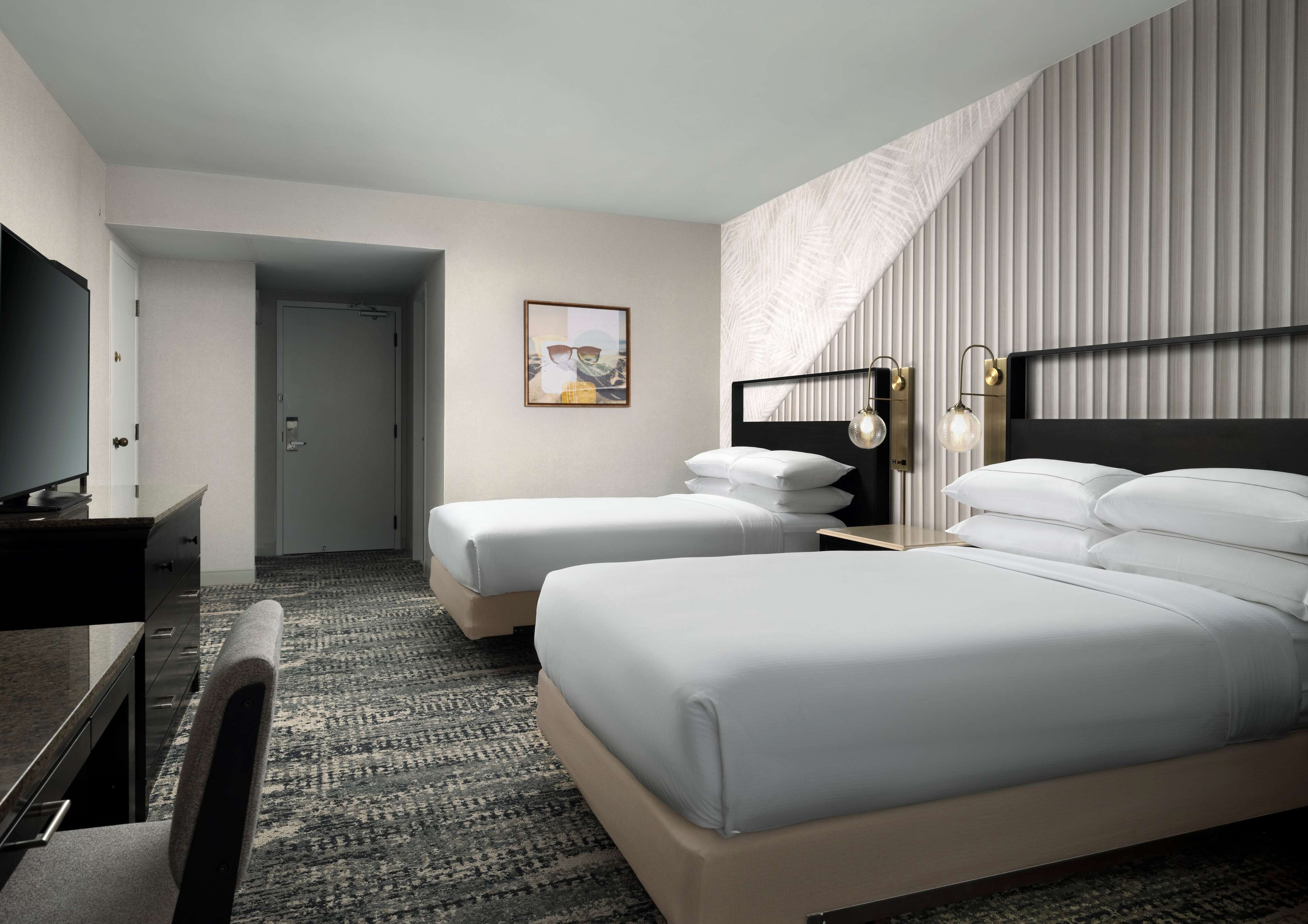 Quarto de hotel com duas camas, uma escrivaninha, uma cadeira e uma televisão.