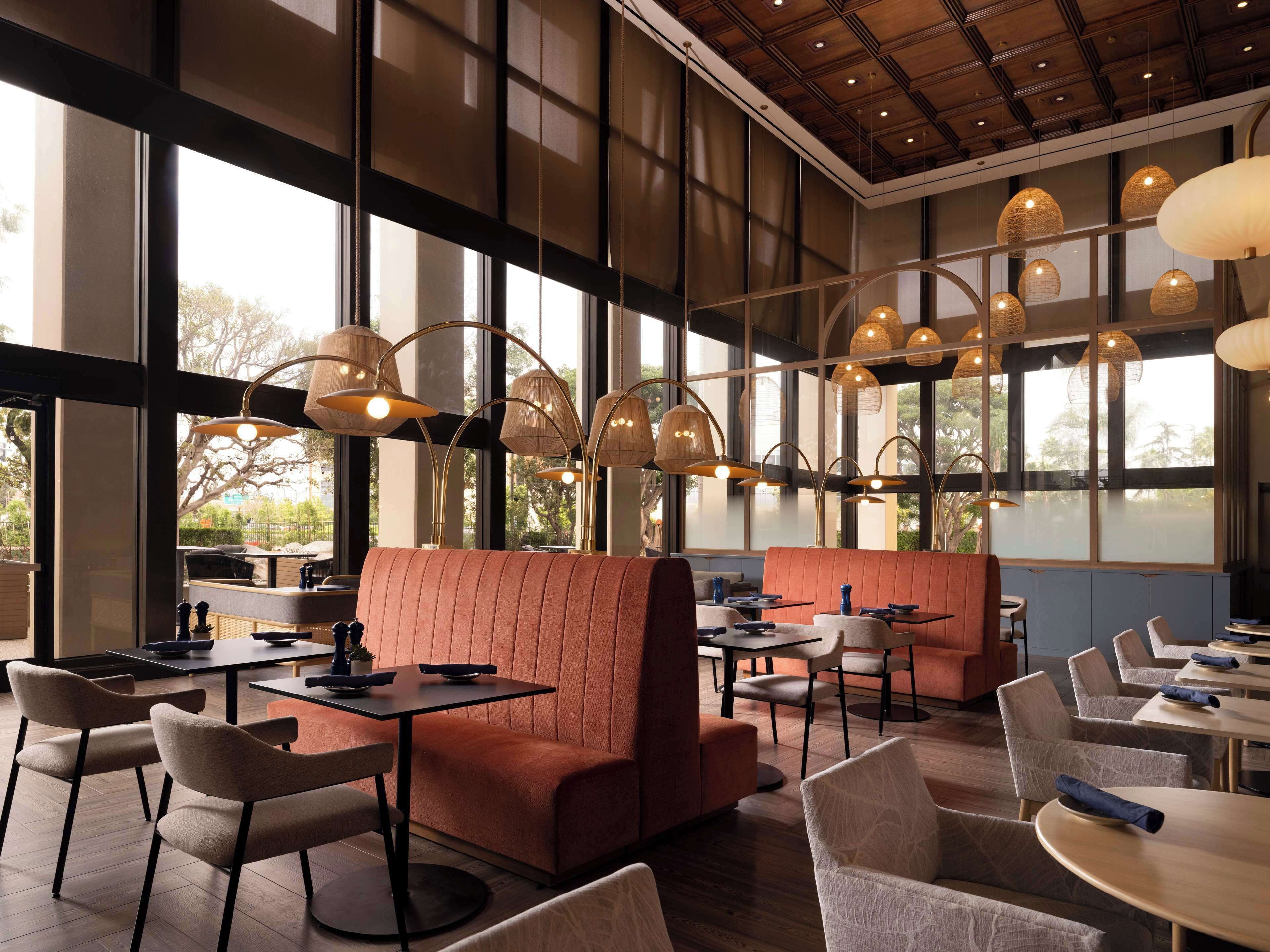Un restaurante moderno con techos altos, amplios ventanales y una variedad de opciones de asientos, incluyendo cabinas y mesas.
