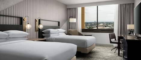 Una habitación de hotel moderna con dos camas, un escritorio y un ventanal que ofrece vistas a la ciudad.
