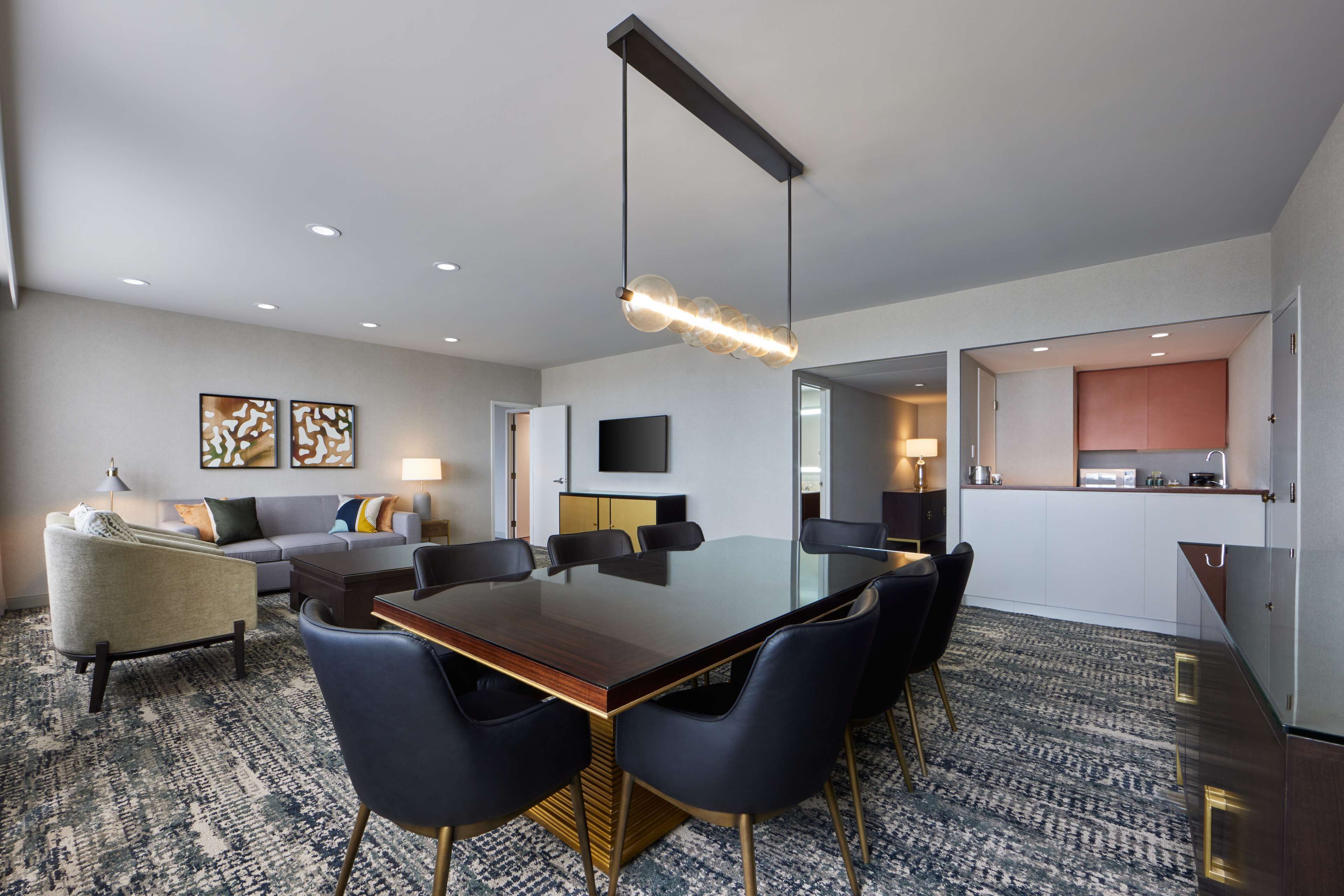 Quarto de hotel moderno com área de refeições, sofá, TV de tela plana e cozinha.