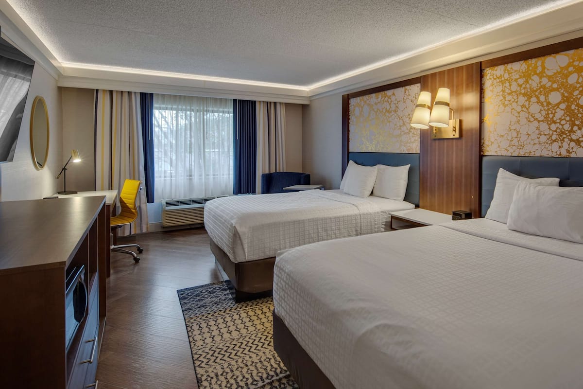 A hotel room with two beds, a desk, a chair, a mirror, and a window with curtains.