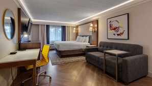 A hotel room with a bed, a desk with a chair, a sofa, a small table, and a large mirror. - The Hub Murray Hill, BW Premier Collection (New Providence)