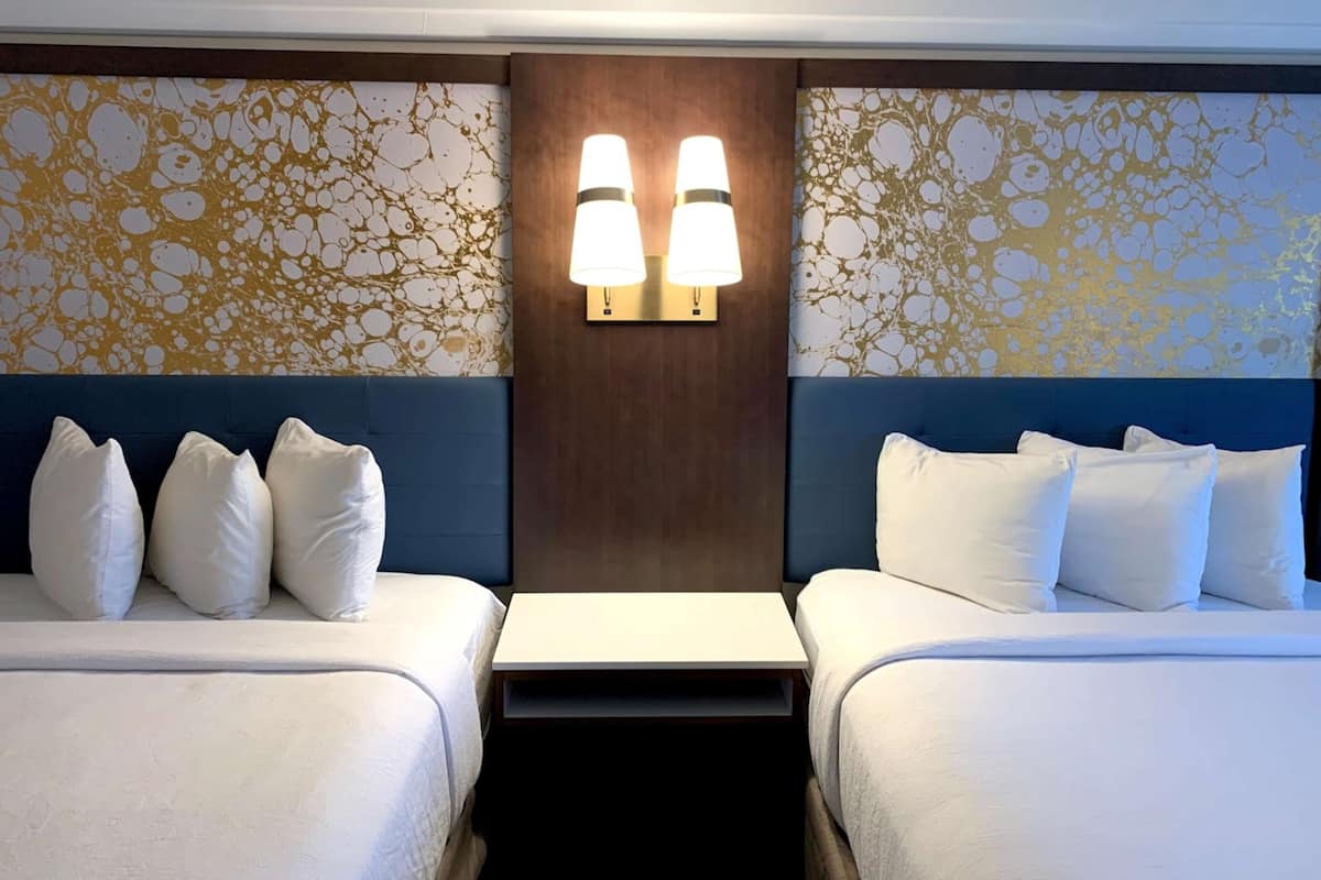 A hotel room with two beds, a nightstand, and a wall-mounted light fixture.
