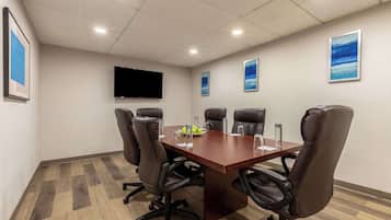 Een vergaderruimte met een houten tafel, zes leren stoelen, een flatscreen televisie en kunstwerken in lijsten aan de muren.