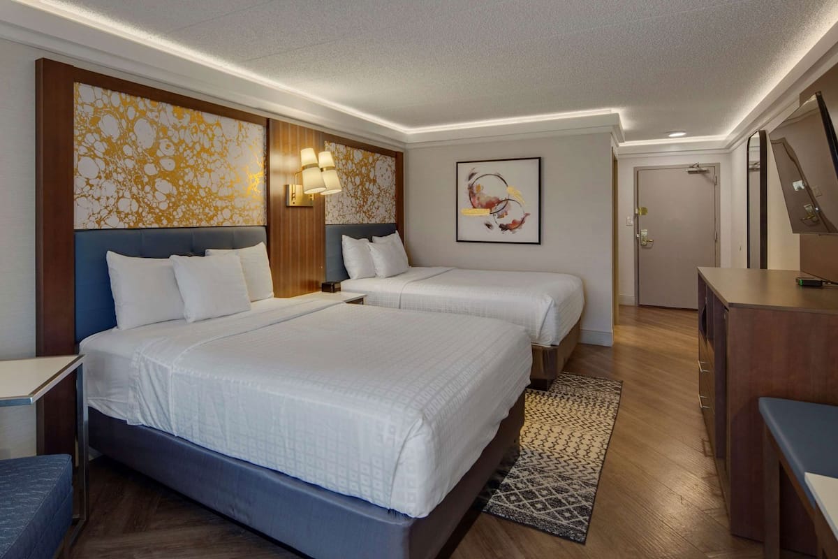 A hotel room with two beds, a desk, a chair, a wardrobe, and a bathroom.