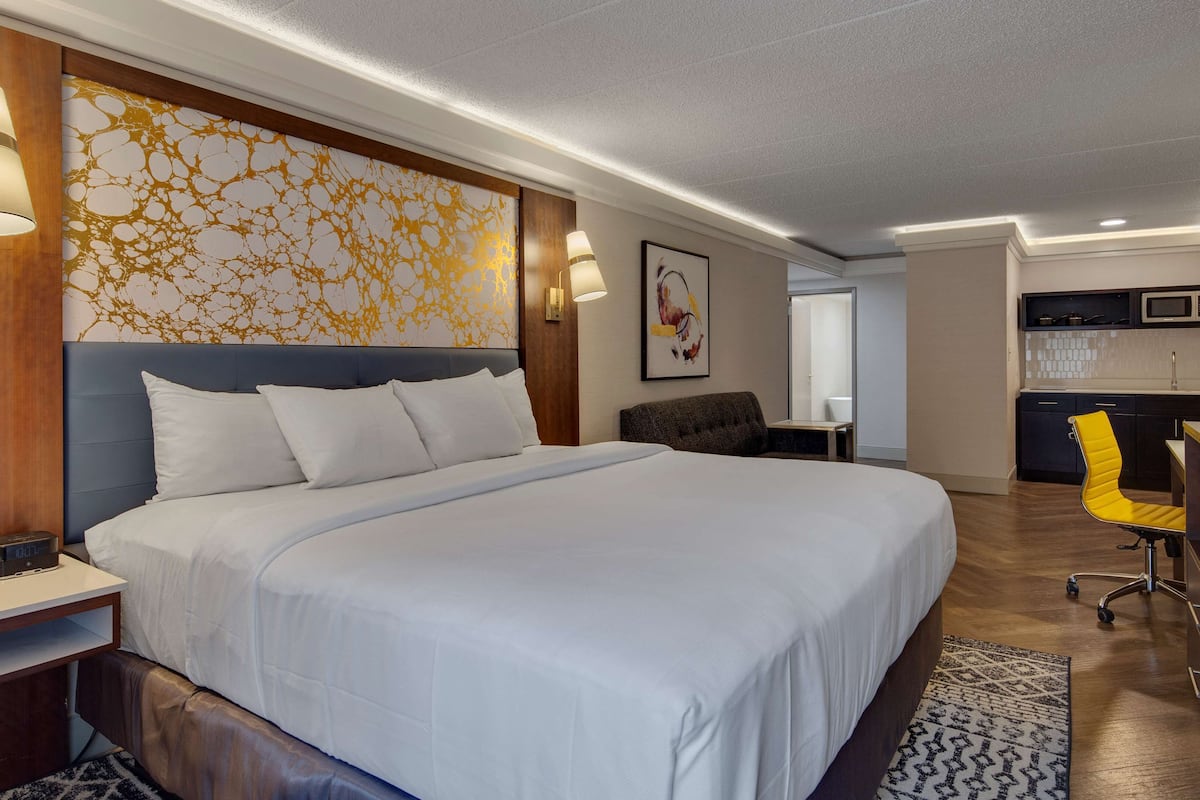 A hotel room with a large bed, bedside tables, a desk, a chair, a microwave, and a small kitchenette.