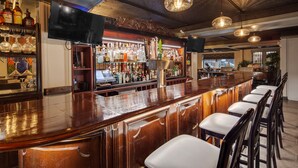 A bar area with a long counter, multiple liquor bottles, and a television screen. - The Hub Murray Hill, BW Premier Collection (New Providence)