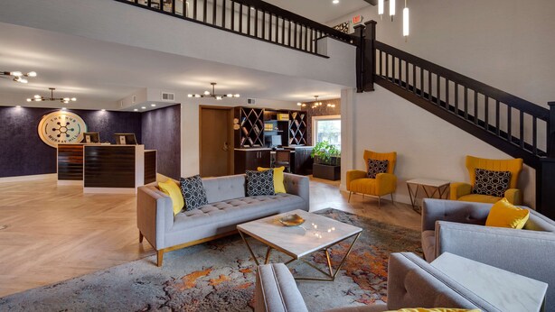 A spacious living area with a grey sofa, yellow armchairs, and a coffee table. A staircase with a black railing leads to an upper level. - The Hub Murray Hill, BW Premier Collection (New Providence)