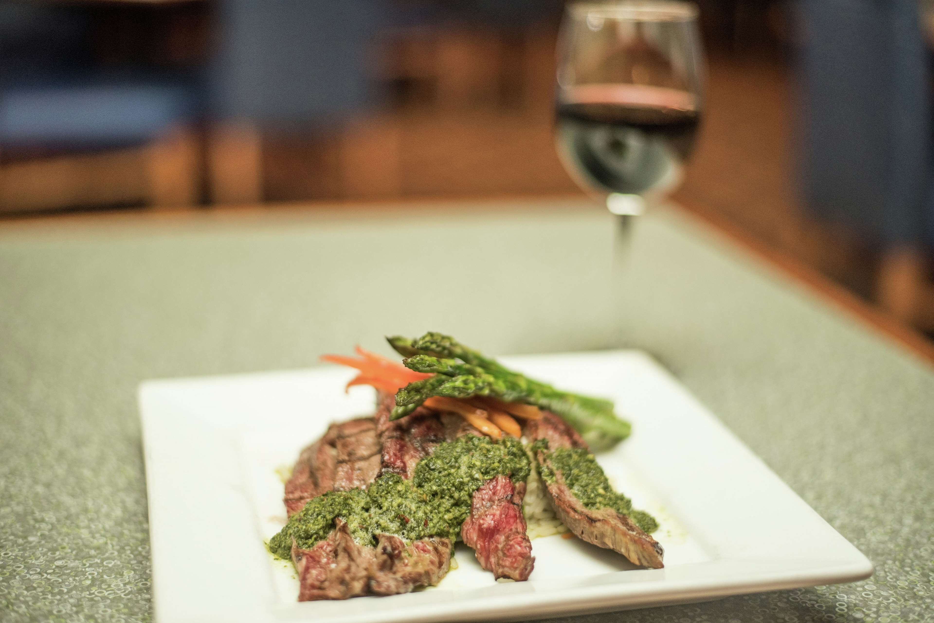 Un piatto di bistecca con salsa verde e verdure su un piatto bianco.