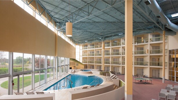 An indoor swimming pool with a view of the outdoors, surrounded by multiple balconies and a high ceiling.
