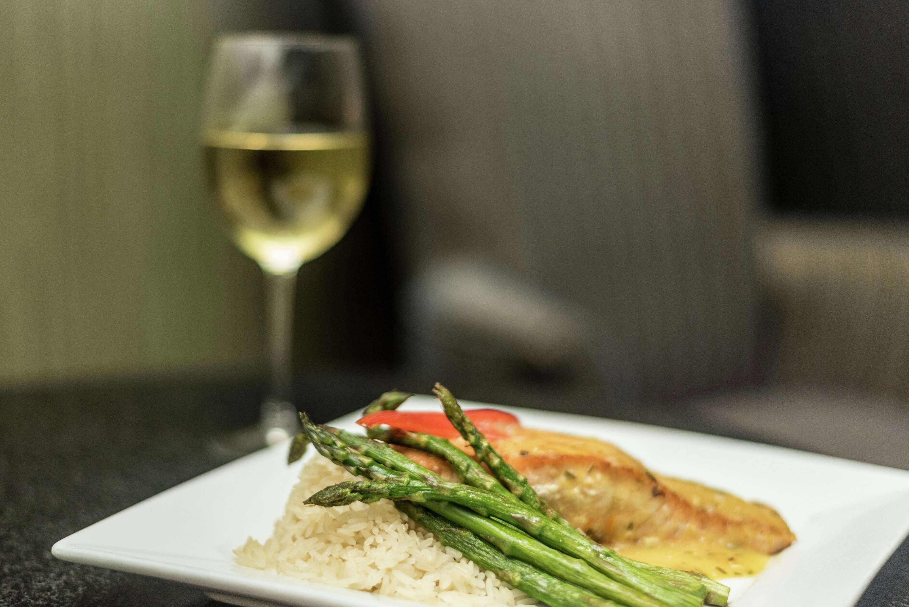 Une assiette de nourriture composée de riz, d’asperges et d’un morceau de poisson, accompagnée d’un verre de vin blanc.