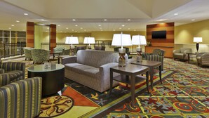 A hotel lobby with a sofa, armchairs, a coffee table, and a TV mounted on the wall.