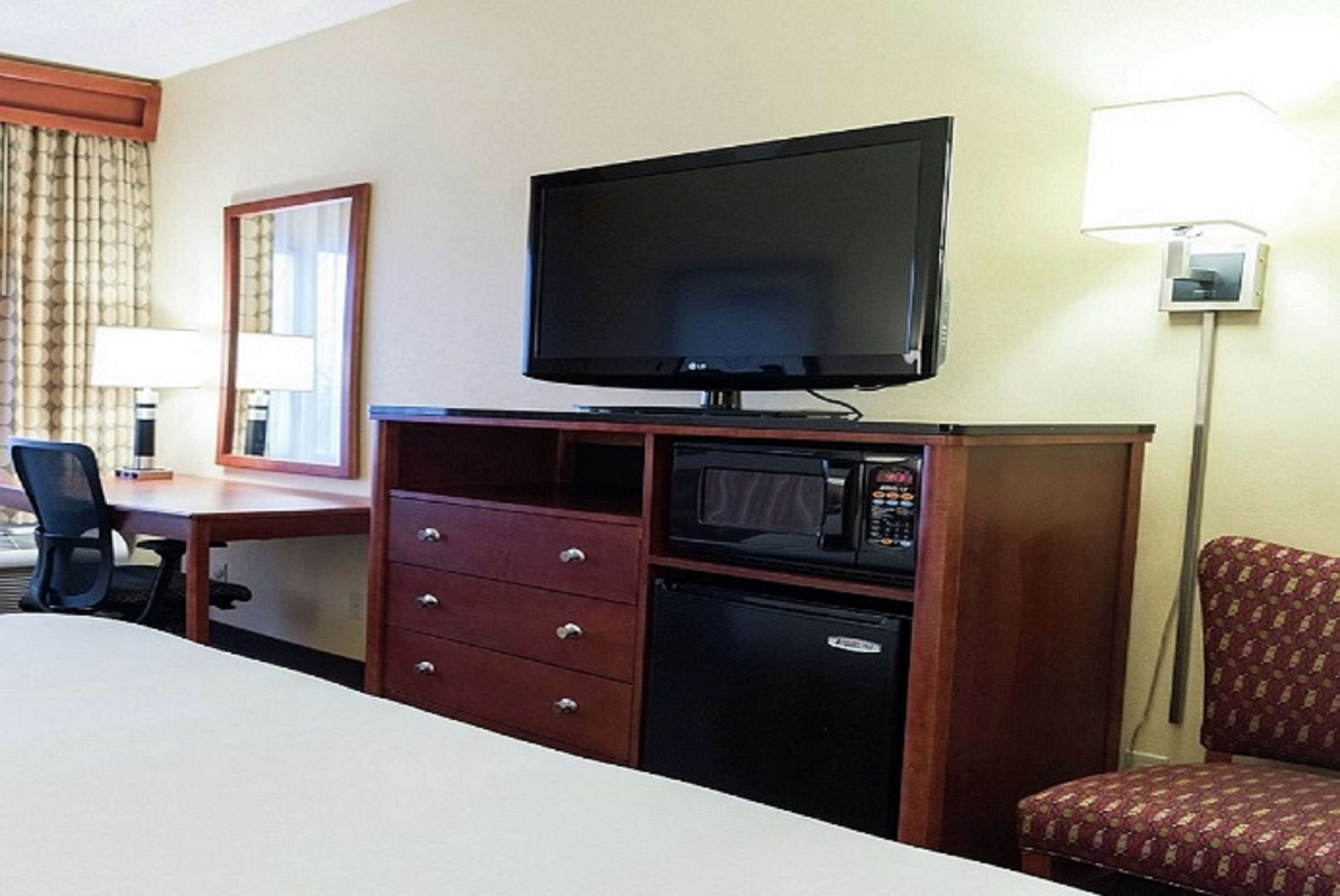 A hotel room with a bed, a desk with a chair, a television, a microwave, and a small refrigerator.