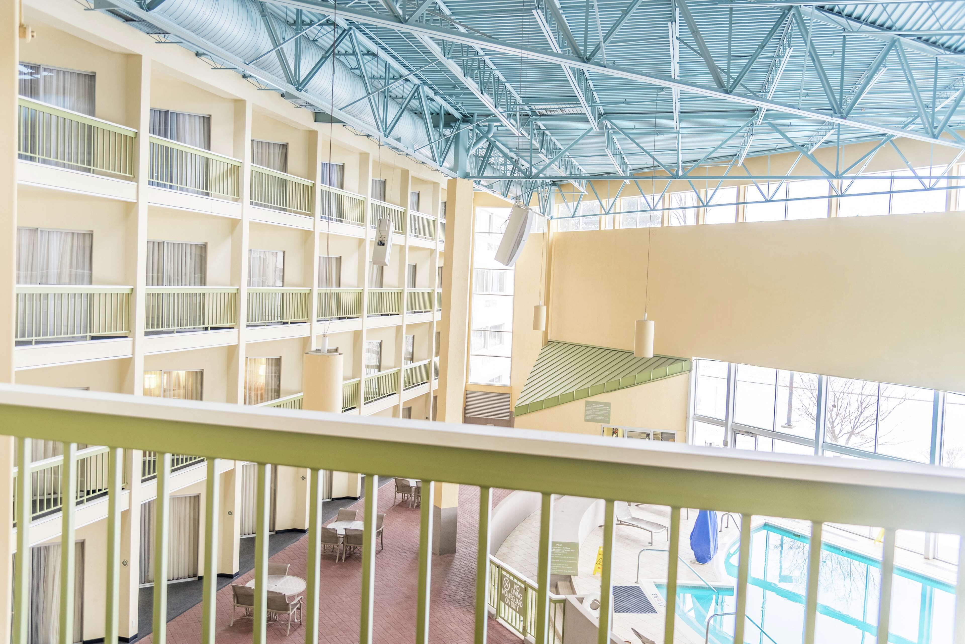 A multi-level hotel interior with balconies, a swimming pool, and a high ceiling with metal beams.