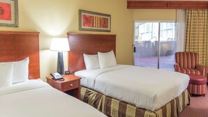 A hotel room with two beds, a nightstand with a telephone, a window with curtains, and a chair.