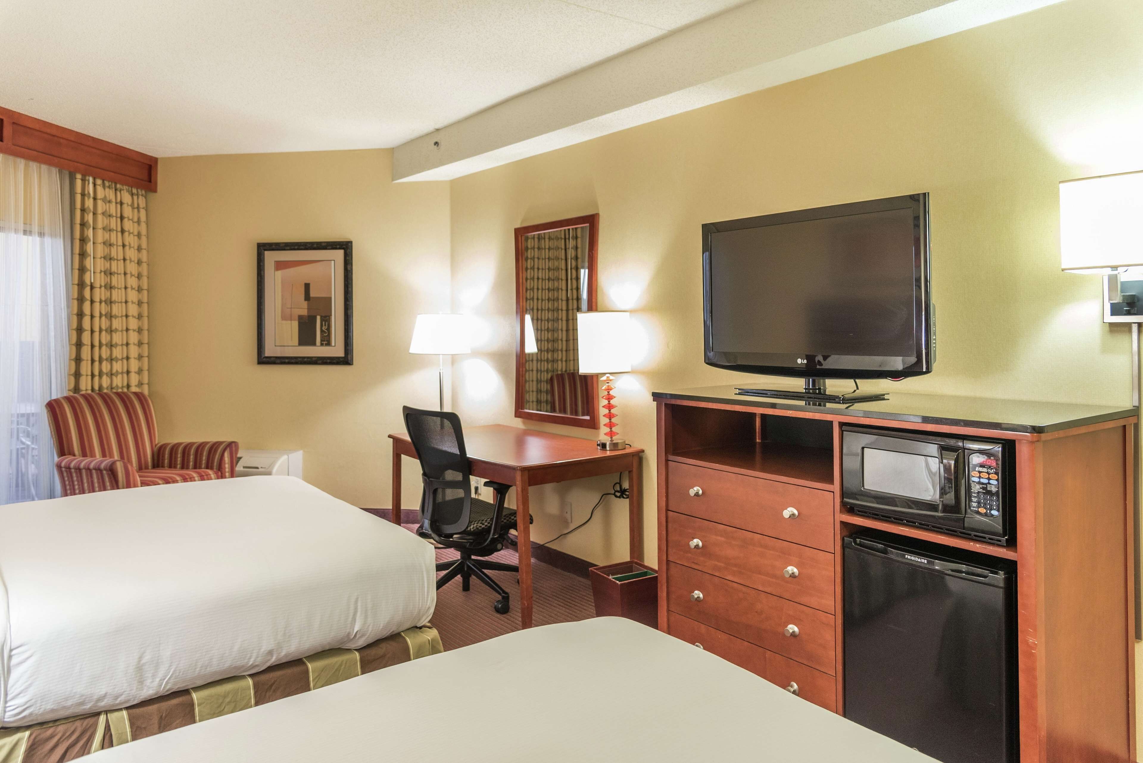 A hotel room with two beds, a desk with a chair, a television, a microwave, and a lamp.
