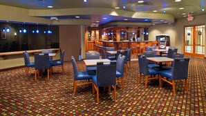 A hotel lobby with a patterned carpet, blue upholstered chairs, and a bar area with a television.