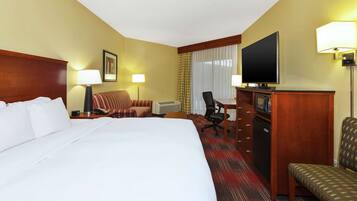 Een hotelkamer met een groot bed, een bureau met een televisie, een stoel en een klein tafeltje.