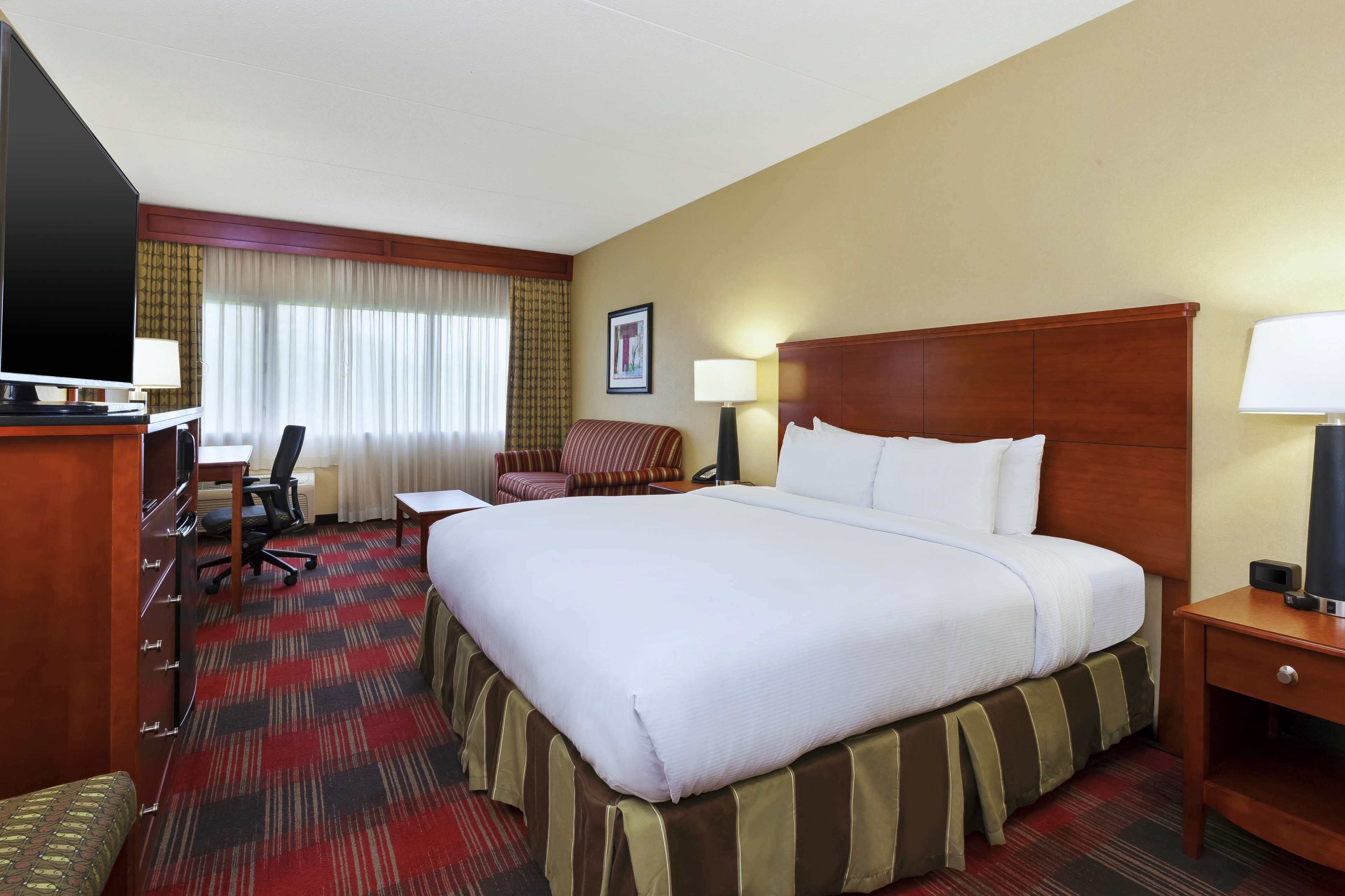 A hotel room with a large bed, a desk with a chair, a television, and a lamp.