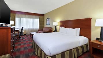 A hotel room with a large bed, a desk with a chair, a television, and a lamp.