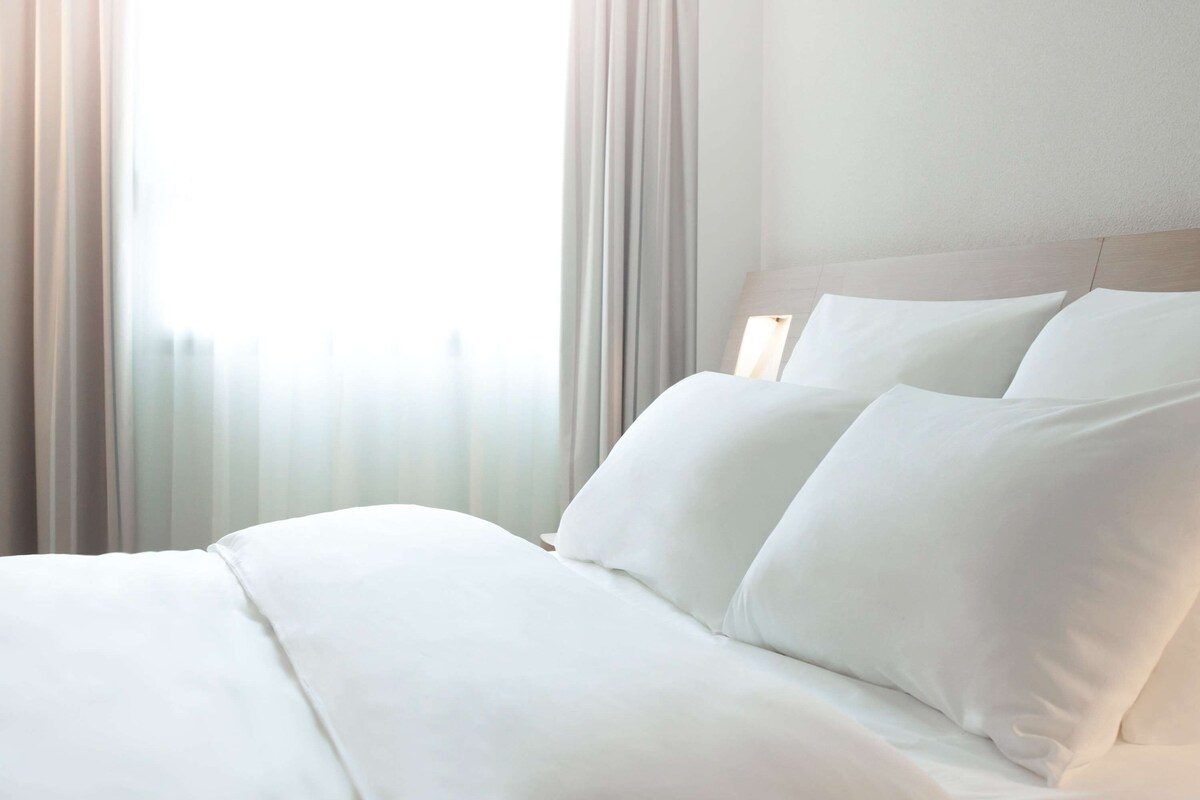 Un lit bien fait, avec du linge de lit blanc, dans une chambre d’hôtel.