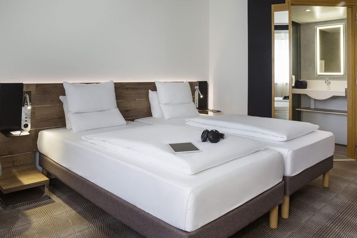 A double bed with white linens, a bedside table with a lamp, and a mirror above the sink.