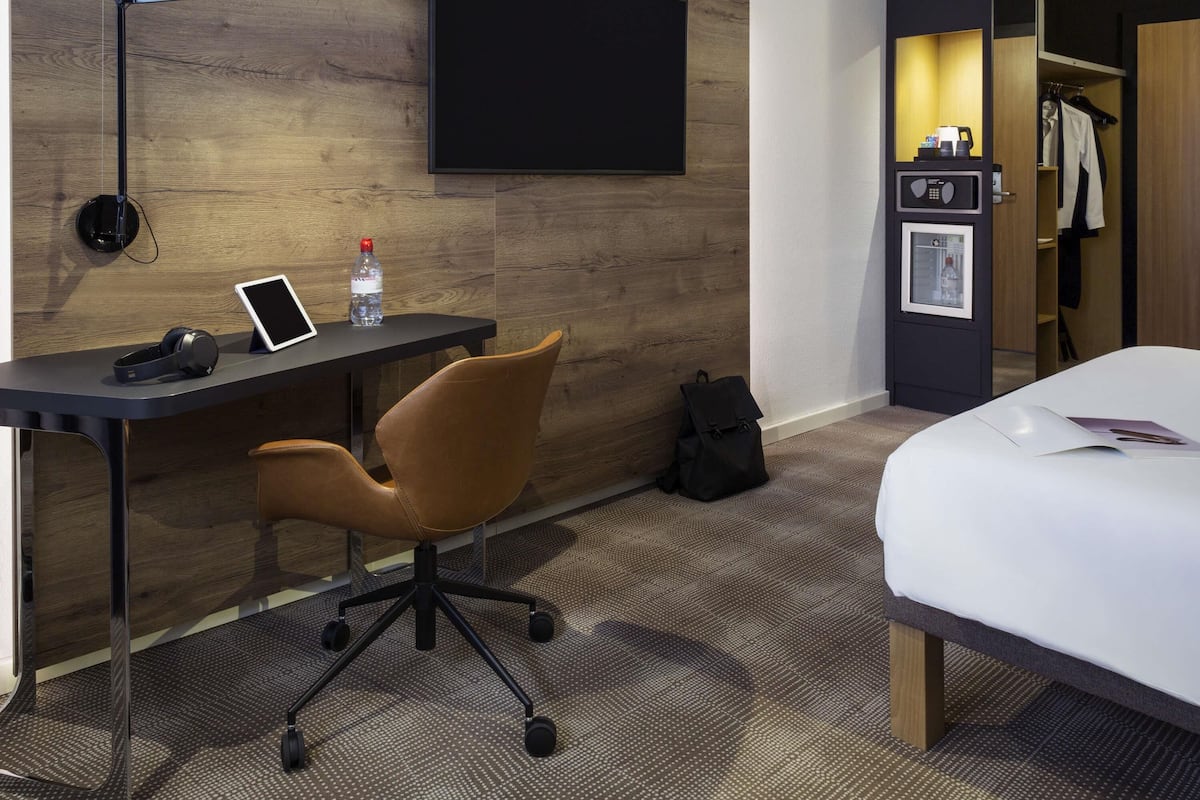 A hotel room with a desk, chair, bed, and a TV mounted on the wall.