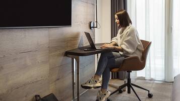 A person sitting at a desk with a laptop in a room with a wooden wall and a projector screen.